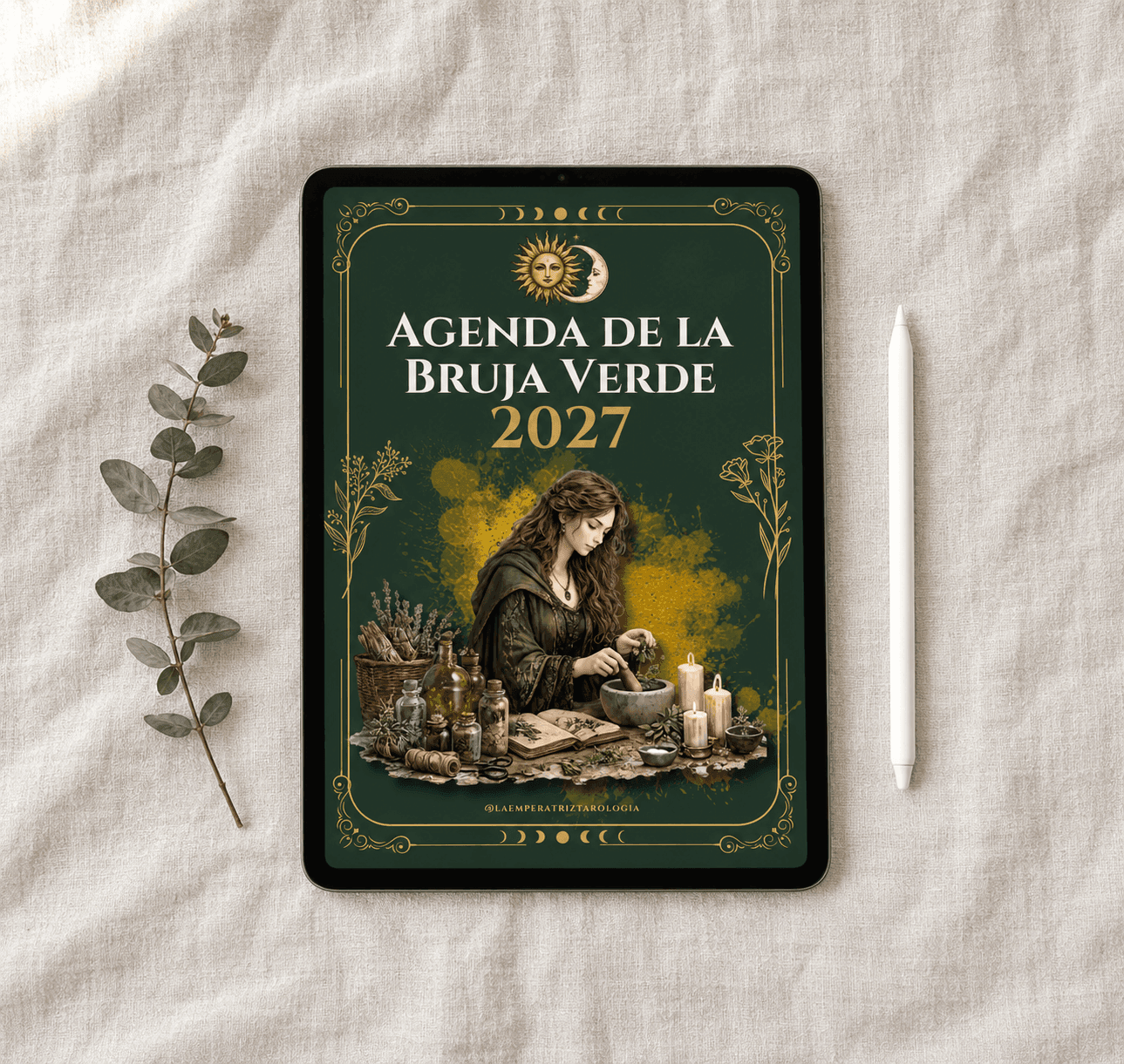 Mockup de la Agenda de la Bruja Verde 2027 abierta en un iPad sobre una tela de lino clara, con un lápiz digital y una rama de eucalipto al costado.